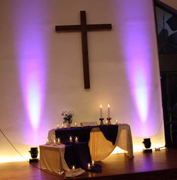 Altarraum mit Kerzen und zwei lila Scheinwerfern