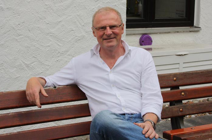 Pastor Clemens Klingel sitzt relaxed auf der Bank vor dem Gemeindezentrum der EmK Neuenhain